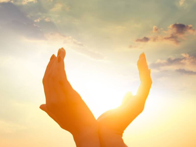 Hände formen ein Herz vor einem Sonnenuntergangshimmel oder Sonnenaufgangshimmel als Symbol für Glaube