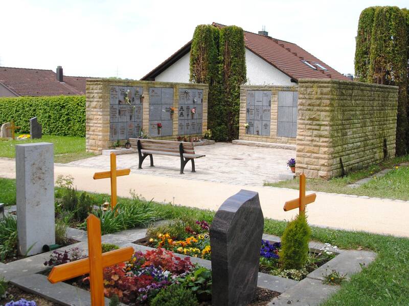 Friedhof mit Grabsteinen im Vordergrund und einer Urnenwand im Hintergrund