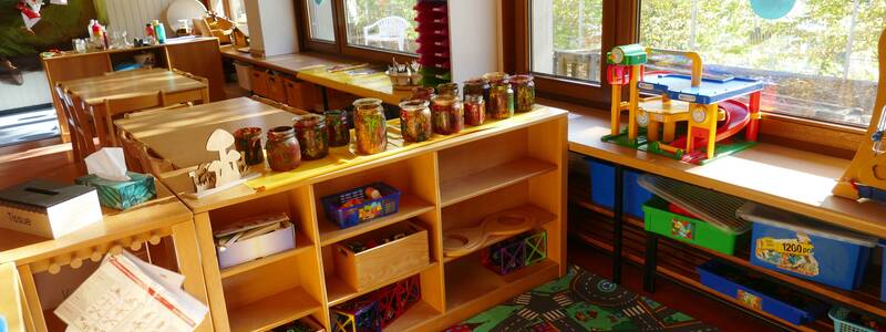 Gruppenraum im Kindergarten Sonnenschein Bünzwangen mit Holzregalen mit Spielsachen und einem Spielteppich mit Straßenlandschaft