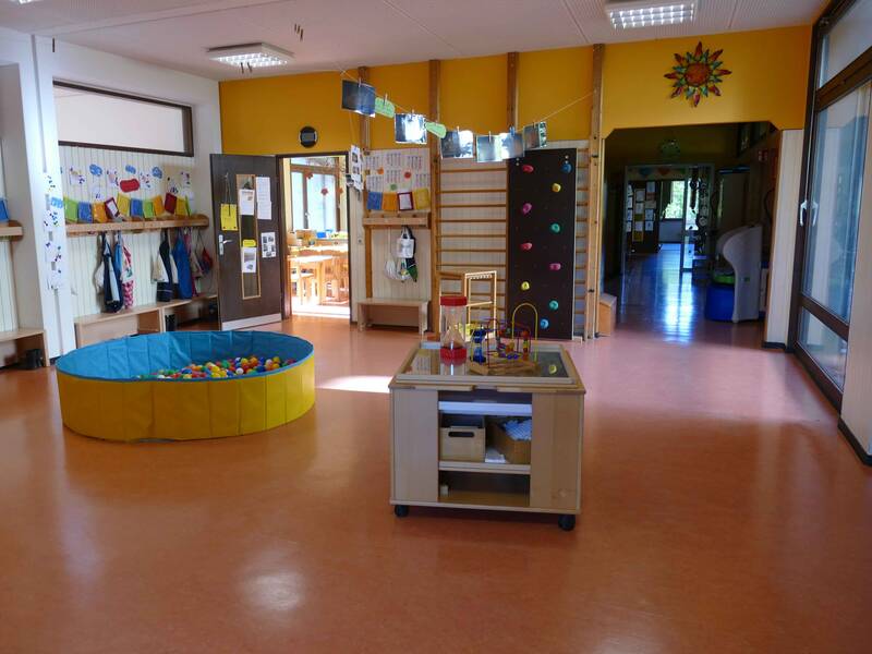 Garderobenbereich im Kindergarten Sonnenschein Bünzwangen mit einem Bällebad in der Mitte des Raumes und einen Rollcontainer aus Holz mit Spielsachen, an der Wand eine Sprossenwand und eine Kletterwand