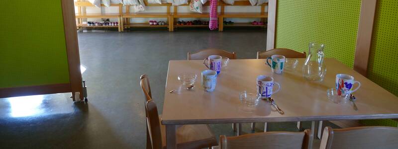 gedeckter Tisch für das Mittagessen im Foyer-Bereich der Kreativkita Die Kunstwerker, im Hintergrund der Garderobenbereich der Regebnofengruppe