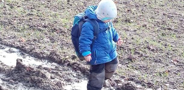 Warm angezogenes Kind des Fuchskinder Naturkindergarten Roßwälden bei einem Spaziergang in einer Matschpfütze